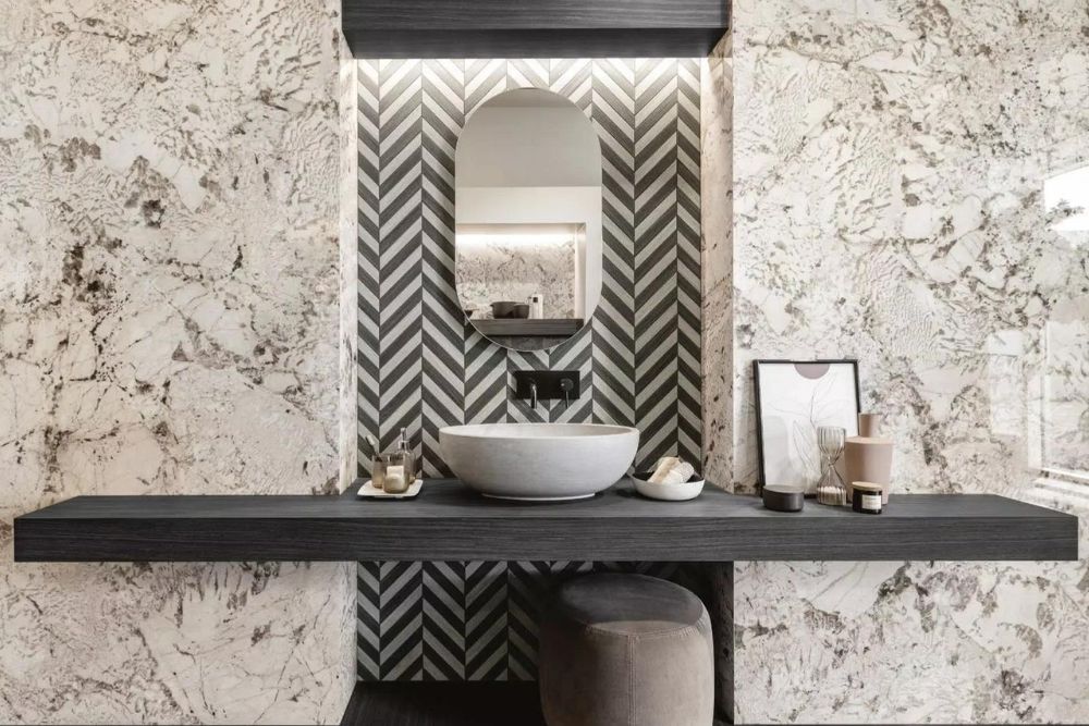 Bancada de casa de banho com espelho e papel de parede com padrão cinzento e branco.