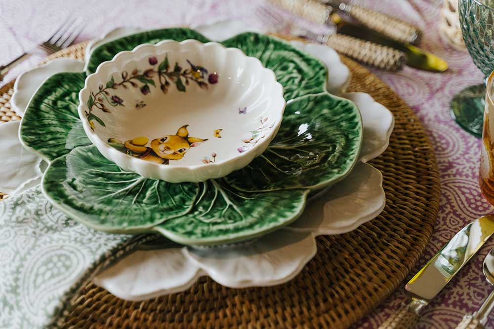 Mesa composta por um prato em forma de couve e taça com coelho da Páscoa e borboletas colocados em cima de um individual redondo em Rattan.