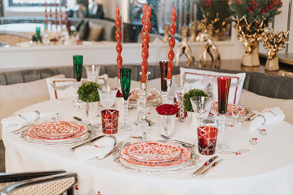 Mesa da consoada composta por copos, pratos com detalhes em branco e vermelho e velas vermelhas.