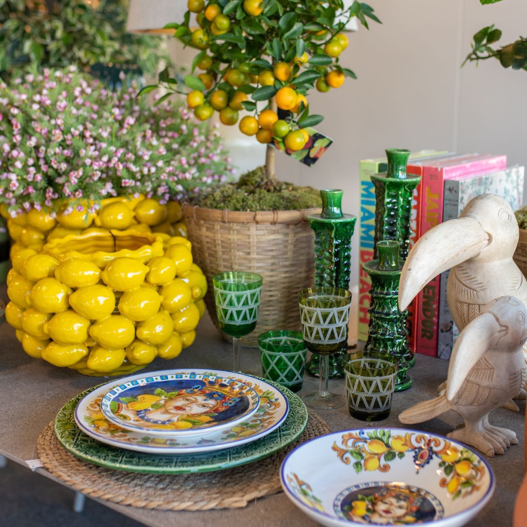 Mesa com serviço de mesa colorido, individual em rattan, copos verdes com detalhes brancos e taça amarela com limões.