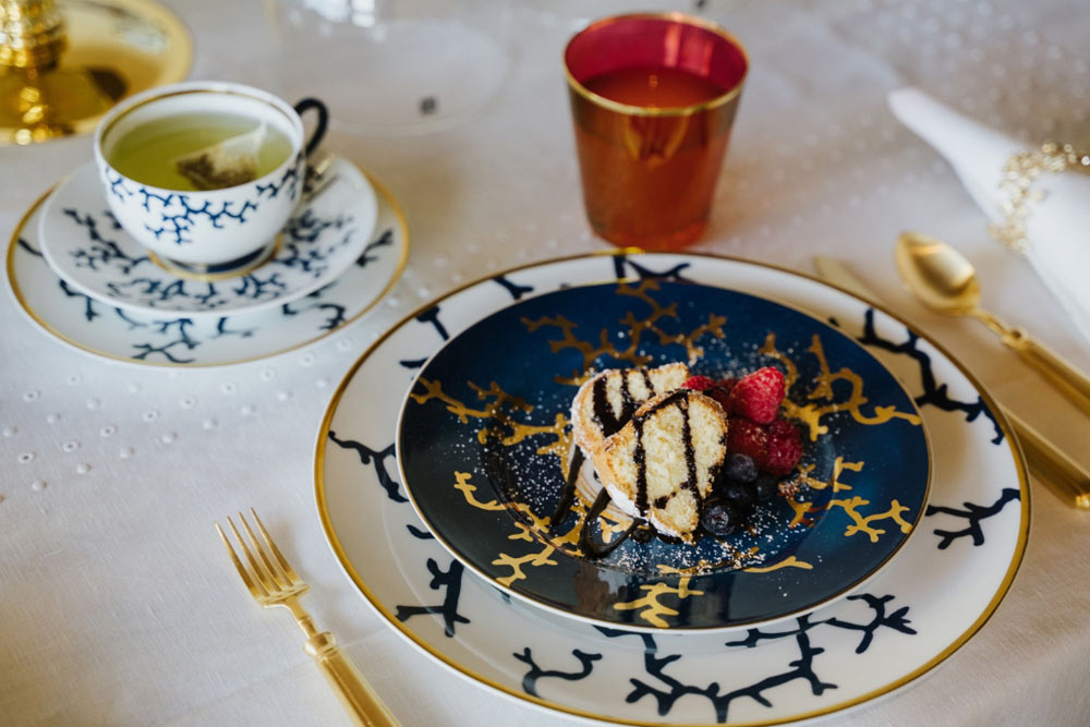 Mesa com prato de sobremesa e prato marcador da marca Raynaud com detalhes elegantes em dourado, branco e azul.